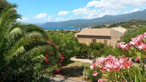 Un edificio con tetto in tegole, circondato dal verde e con vista panoramica sul mare e sulle montagne.