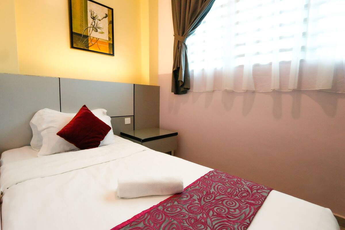 A neatly made bed with a red pillow, a patterned throw, and a headboard against a wall with a framed picture.