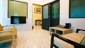 A room with a TV mounted on the wall, a wooden chair, a small table with a coffee maker, and a door with frosted glass panels. - Travelland Hotel (Ipoh)