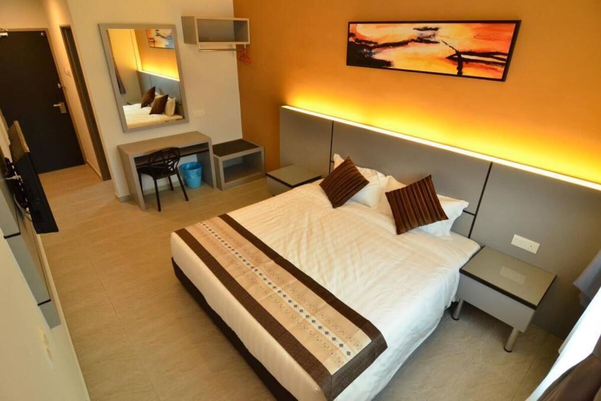 A hotel room with a bed, bedside tables, a desk with a chair, a mirror, and a painting on the wall.