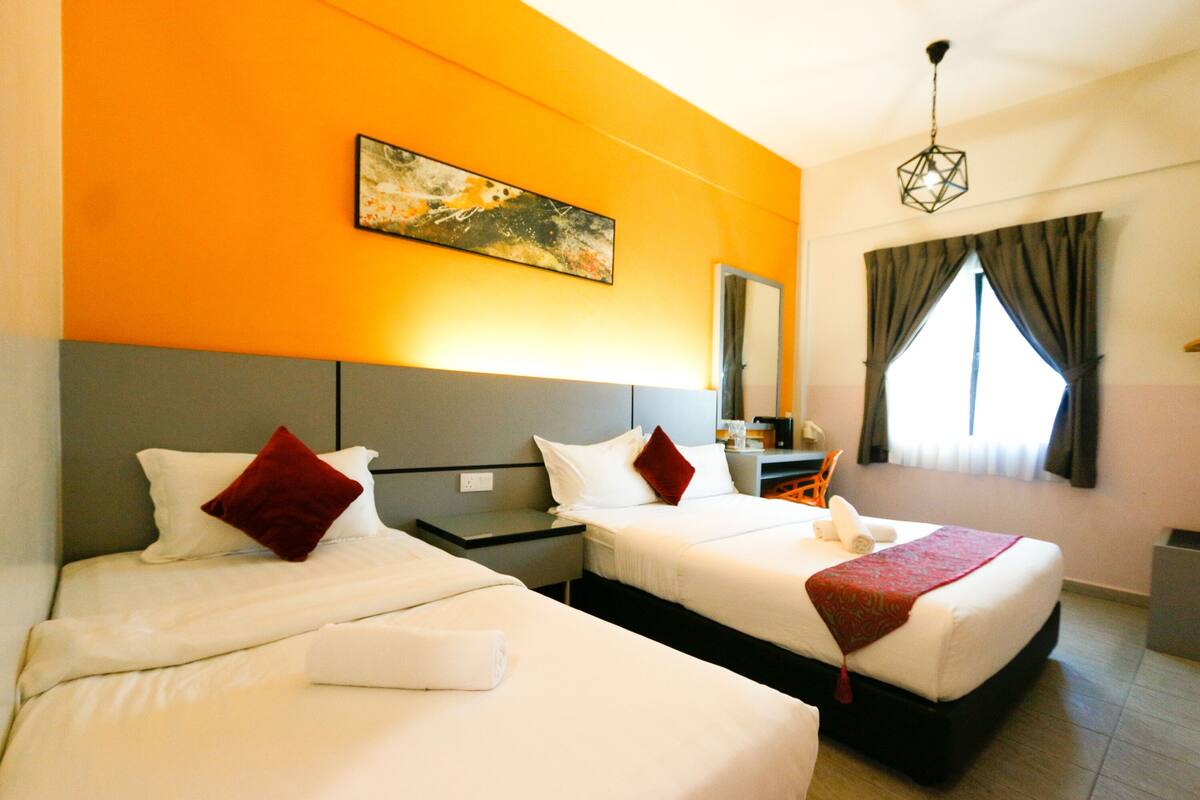 A hotel room with two beds, a painting on the wall, a desk, and a window with curtains.