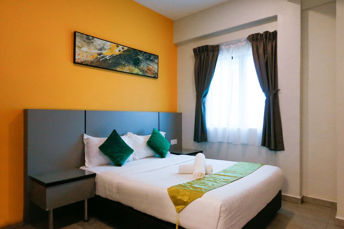 A hotel room with a bed, a nightstand, a painting on the wall, and a window with curtains.