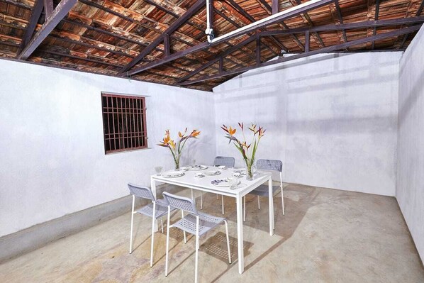 Une table à manger blanche avec quatre chaises, une fenêtre avec des barreaux en métal et un plafond avec des poutres apparentes.