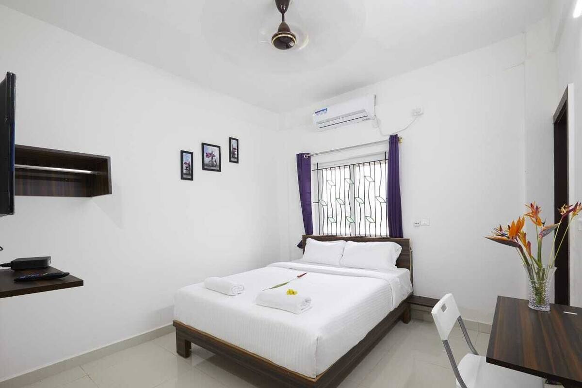 A hotel room with a bed, a desk, a chair, an air conditioner, and a window with curtains.