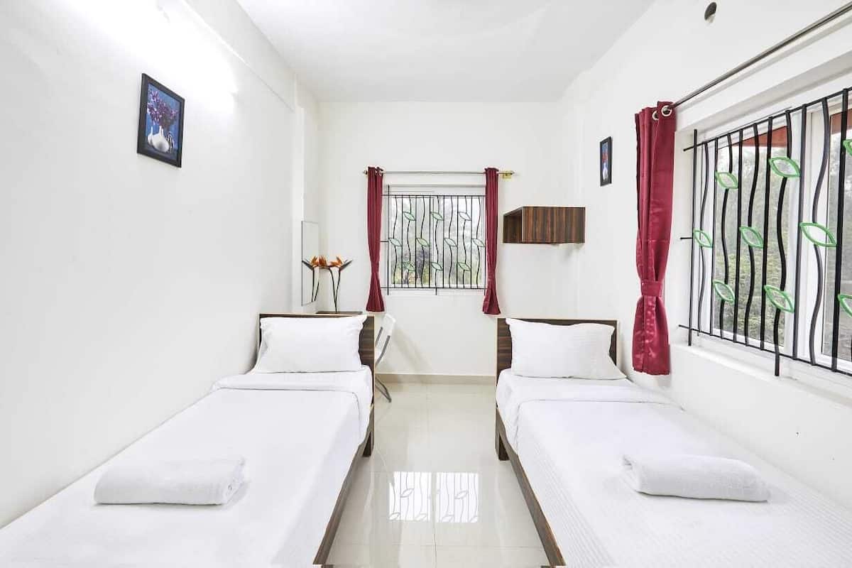 A room with two single beds, a window with metal bars, a small table with a lamp, and a picture on the wall.