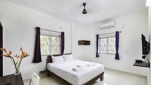Habitación de hotel con cama, escritorio, silla, televisión y ventilador de techo.