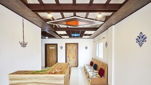 Un moderno vestíbulo de hotel con un mostrador de recepción de madera, un área de descanso con cojines de colores, y un techo con vigas a la vista y luminarias.