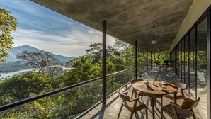 A terrace with a table and chairs, overlooking a mountainous landscape and a body of water. - Elakai Munnar (Udumbanchola)
