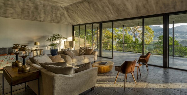 A modern living room with a large window offering a mountain view, a sofa set, a coffee table, and a side table with decorative items.