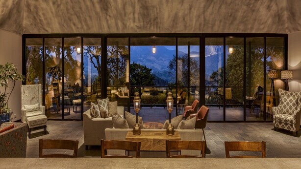 A modern interior with a seating area, large windows, and a view of the outdoors. - Elakai Munnar (Udumbanchola)