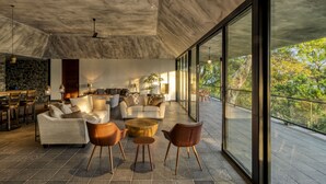 A spacious living area with modern furniture, a stone wall, and large windows offering a view of the outdoors. - Elakai Munnar (Udumbanchola)