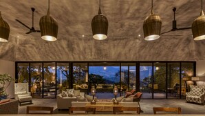A spacious living area with a large window overlooking a scenic landscape, a ceiling fan, and a wooden coffee table. - Elakai Munnar (Udumbanchola)