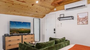 Ein Schlafzimmer mit einem Bett, einem Schminktisch, einem Fernseher und einer Wandklimaanlage.