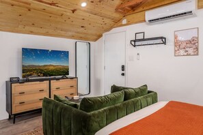 A bedroom with a bed, a dresser, a television, and a wall-mounted air conditioning unit.