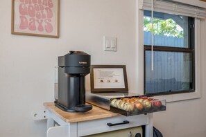 Une machine à café sur un chariot, avec un plateau de dosettes de café, un certificat encadré et une fenêtre avec des stores.
