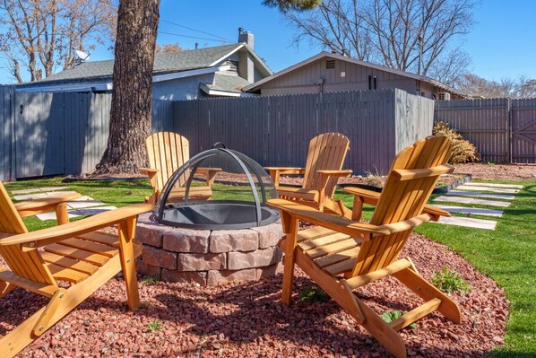 Un jardin avec un foyer en pierre entouré de chaises Adirondack en bois, une terrasse en bois et un jardin clos.
