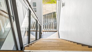 A modern staircase with glass railings and wooden steps leading to an outdoor area.