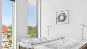 A bedroom with two beds, a large window, and a framed artwork on the wall.