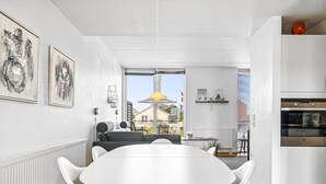 A modern kitchen with white cabinetry, a built-in oven, and a dining area with a white table and chairs.
