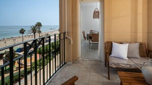 A balcony with a view of the beach, a dining area with a table and chairs, and a small seating area with a table and cushions. - Alborán by Interhome (Estepona)