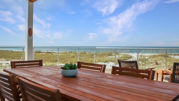 A wooden table with chairs and a potted plant, overlooking a beach with a clear sky. - Sea La Vie (Port St. Joe)