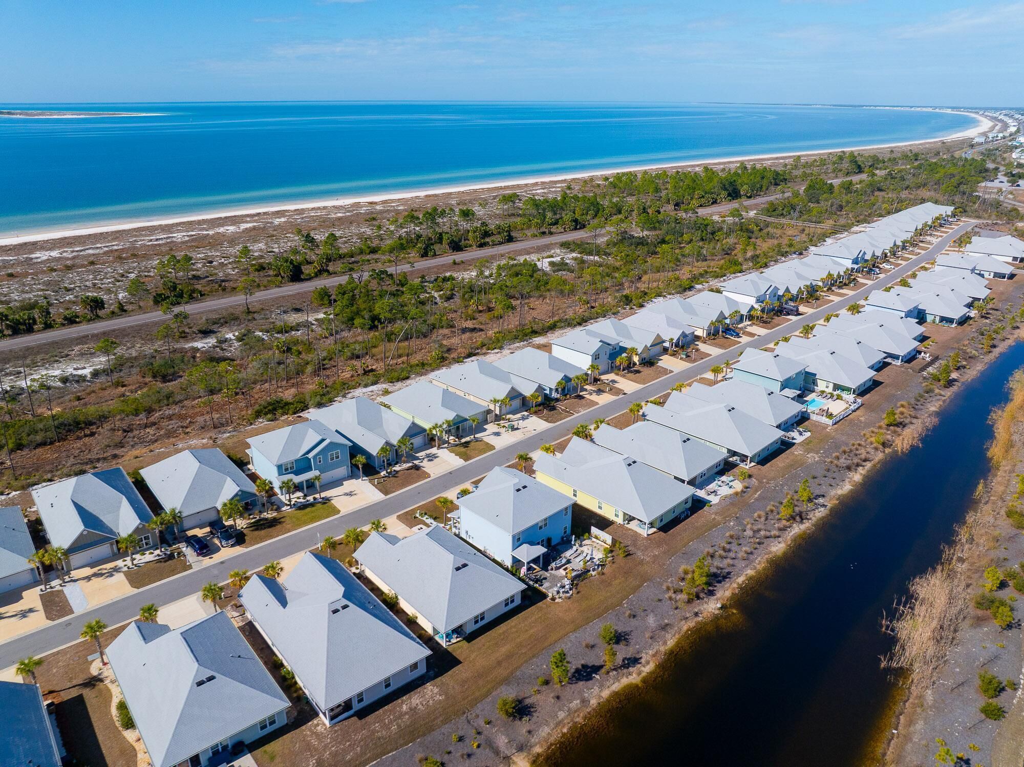 A coastal residential area with a row of modern houses with grey roofs, a beach, and a river.