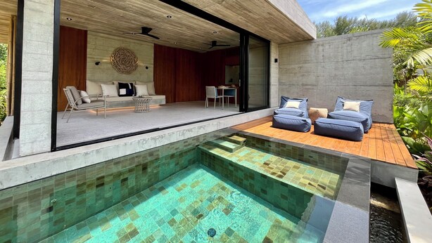 Un espace de vie extérieur moderne, doté d’une piscine, de coins salon et offrant une vue sur l’intérieur.