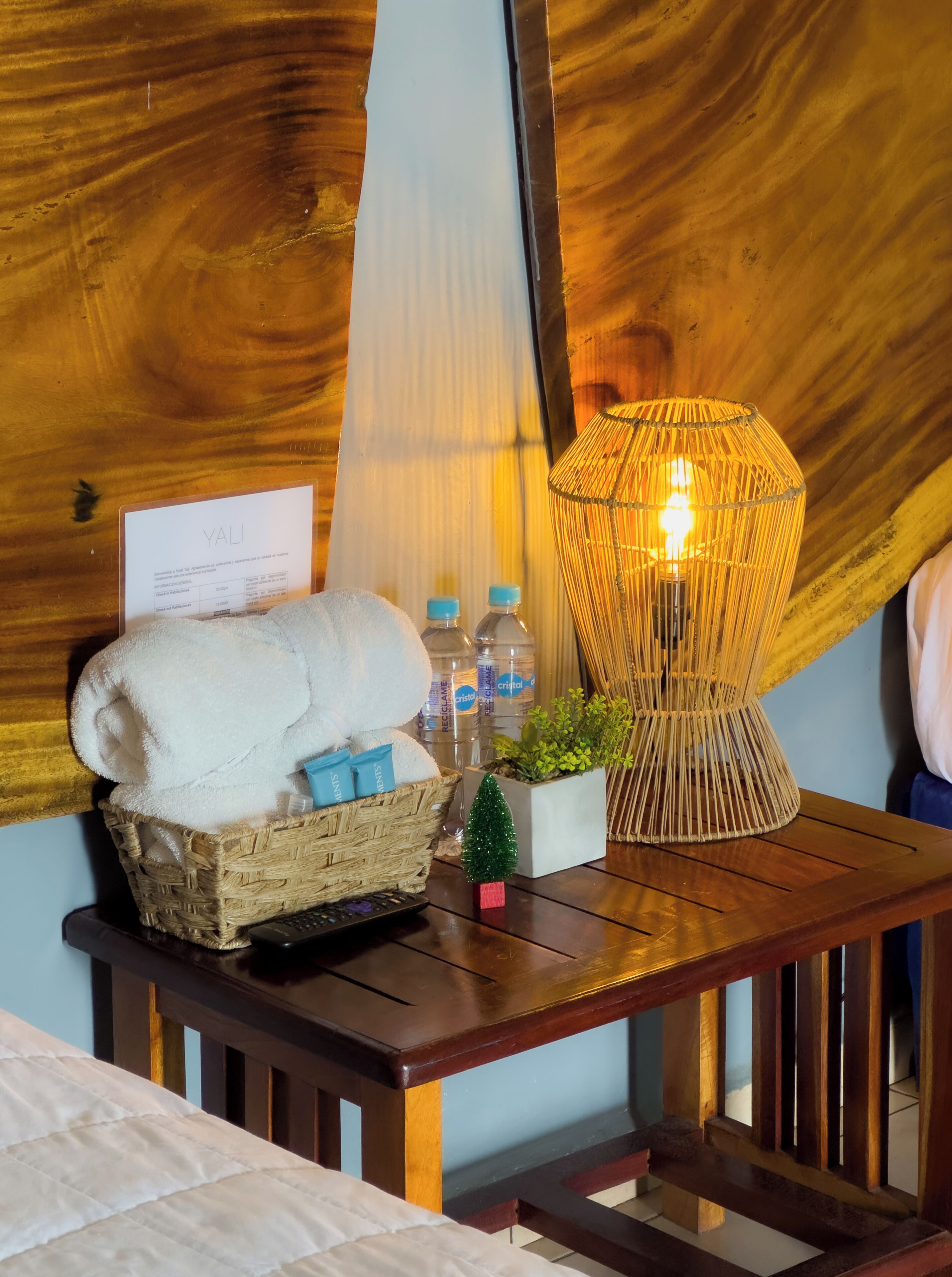 Una mesa de madera con una cesta de toallas, una planta pequeña y una lámpara.