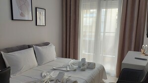 Habitación de hotel con cama, escritorio y silla. Hay dos cuadros en la pared, una ventana con cortinas y un aire acondicionado.