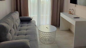 Una sala de estar moderna con un sofá gris, una mesa redonda de centro, un escritorio blanco y un televisor de pantalla plana.