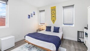 A bedroom with a bed, a nightstand, a lamp, a radiator, and a window with blinds. - Stag Sweet Suite in Capitol Hill (Seattle)