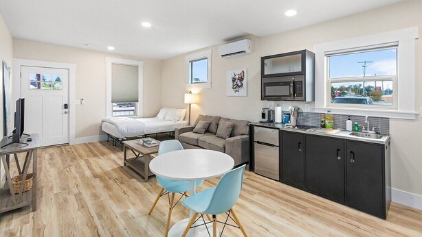 Une chambre d’hôtel de taille réduite comprenant un lit, un canapé, une table à manger avec des chaises, un coin cuisine et une fenêtre donnant sur un paysage agréable.