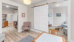 A spacious living area with a dining table, a sofa, and a chair. There is a sliding door leading to another room, and a kitchen area is visible in the background. - The Night Owl Perch in Stanwood (Stanwood)
