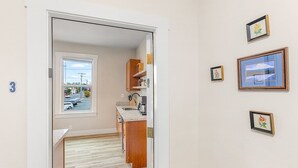 A hallway leading to a kitchen with wooden cabinets and a window. There are framed pictures on the wall. - The Night Owl Perch in Stanwood (Stanwood)