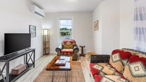 A living room with a flat-screen TV, a sofa, a chair, a coffee table, and a window with a view. - The Nightjar Shelter (Stanwood)