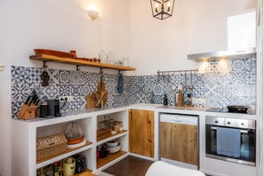 A compact kitchen with a white countertop, wooden cabinets, a built-in oven, and a backsplash with blue and white tiles.