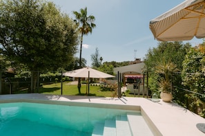 A swimming pool with a white deck, surrounded by greenery and a covered patio area. - Holiday Home 'Casa Familia' with Private Pool, Wi-Fi and Air Conditioning (Sa Pobla)