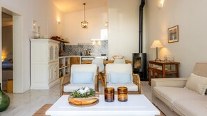 A living room with a white sofa, two armchairs, a coffee table with decorative items, a fireplace, and a kitchen in the background. - Holiday Home 'Casa Familia' with Private Pool, Wi-Fi and Air Conditioning (Sa Pobla)