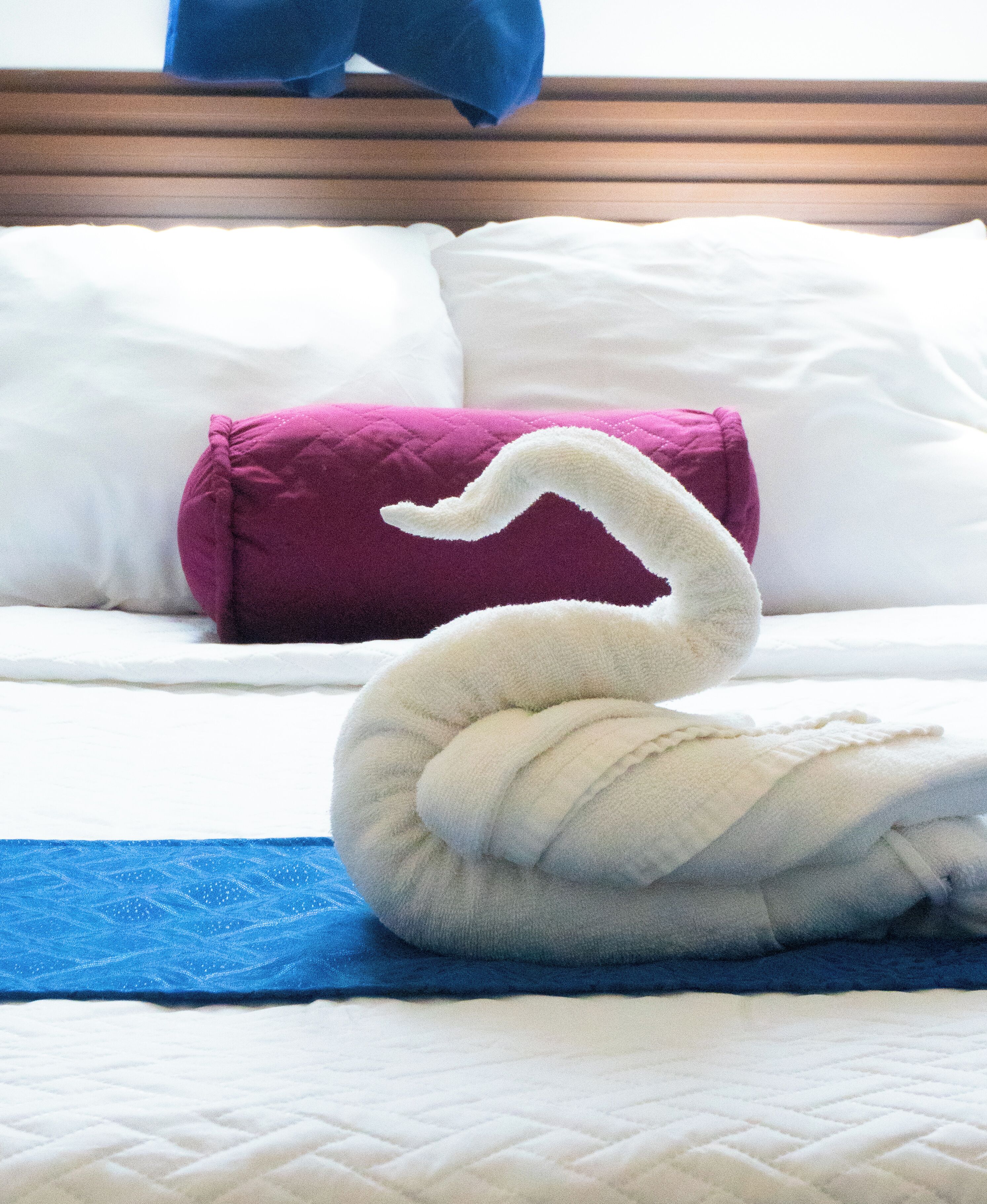 Un lit avec une serviette en forme de cygne et une serviette bleue sur un couvre-lit blanc.