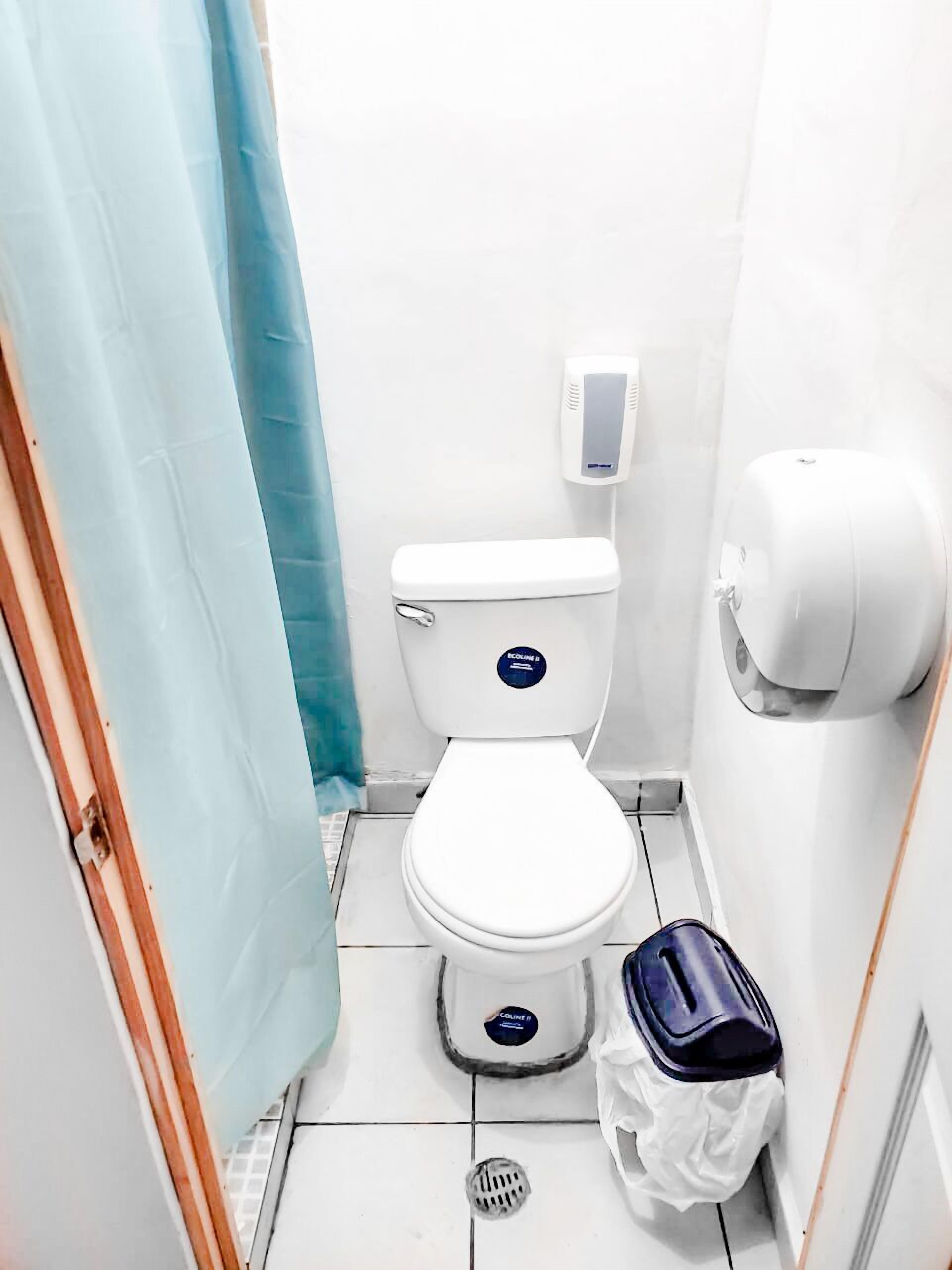 Une petite salle de bain propre, équipée de toilettes, d’un distributeur de gel hydroalcoolique et d’une poubelle.