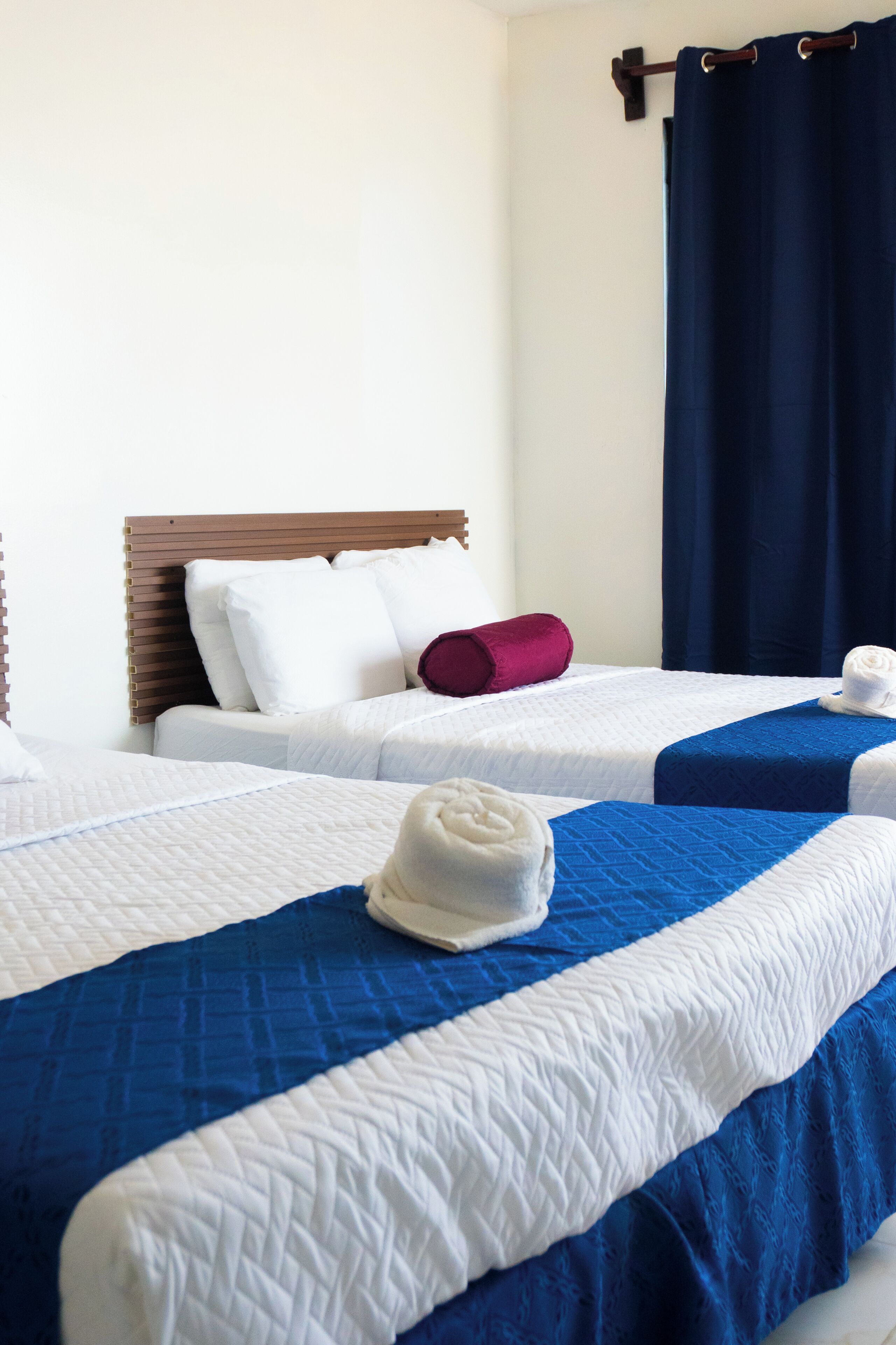 A hotel room with two beds, each with a blue and white bedspread, a wooden headboard, and white pillows.