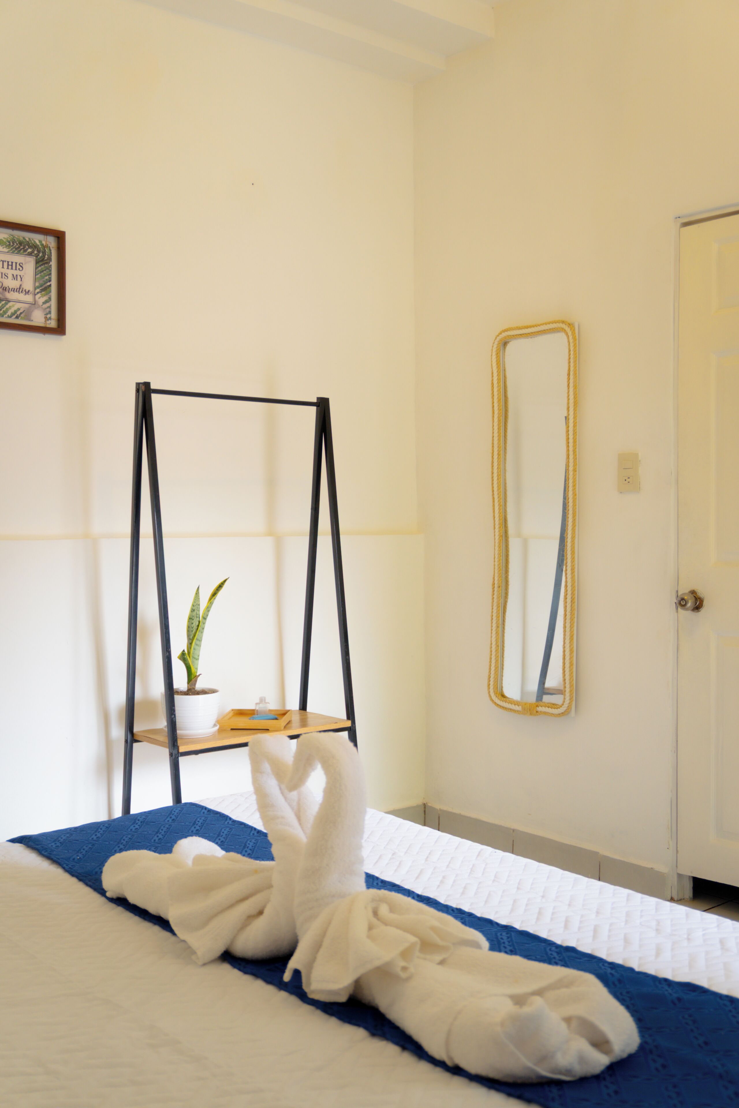 Une chambre d’hôtel avec un lit, un fauteuil suspendu, un miroir et une petite plante.