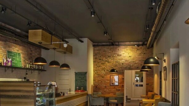 A modern restaurant interior with exposed brick walls, wooden tables, and blue chairs. - Central Hostel (Sheki)