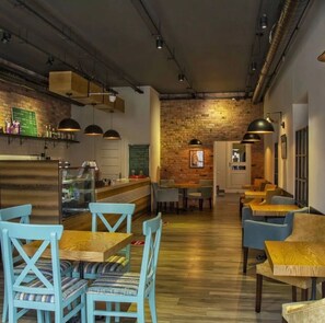 A modern restaurant interior with exposed brick walls, wooden tables, and blue chairs. - Central Hostel (Sheki)
