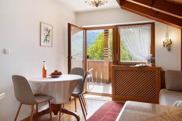 A dining area with a table, chairs, a red rug, a wooden partition, and a view of a balcony with a door.