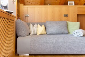 A wooden ceiling, a grey sofa with pillows, and a wooden floor.