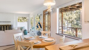 Un coin repas avec une table en bois dressée pour quatre personnes, des chaises blanches et une grande fenêtre donnant sur la forêt.