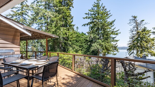Une terrasse en bois avec une table et des chaises, donnant sur un lac bordé d’arbres.