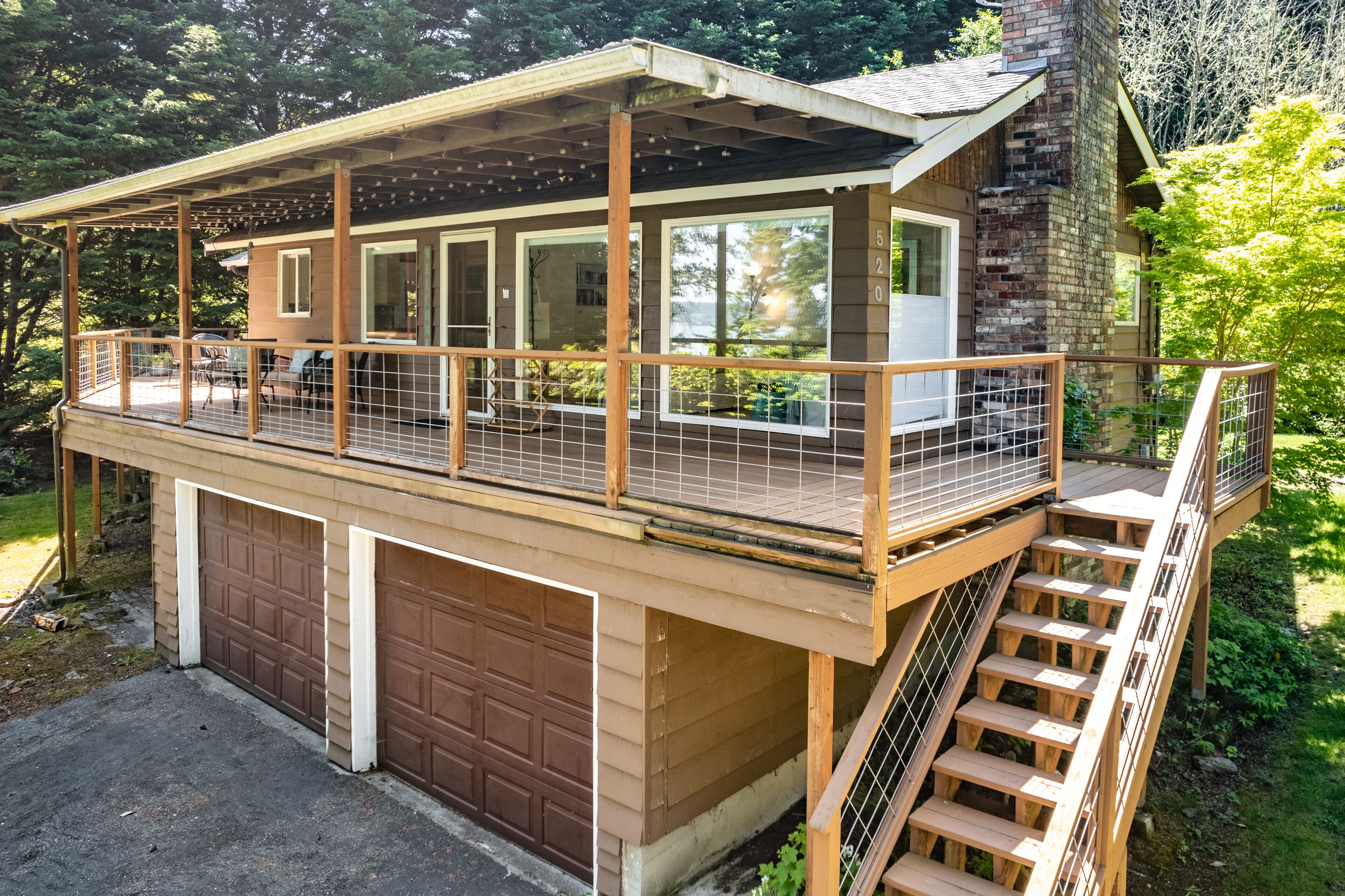 A two-story wooden deck with a covered area, a garage, and a staircase leading to the upper level.