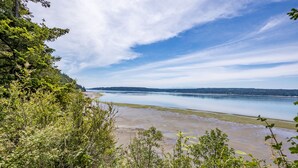 A river with a sandy shore, surrounded by dense greenery and a clear sky. - The Cottage at Herons Roost by AvantStay (Langley)